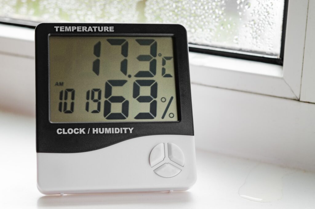 hygrometer with a thermometer stands on a windowsill with drops of condensate