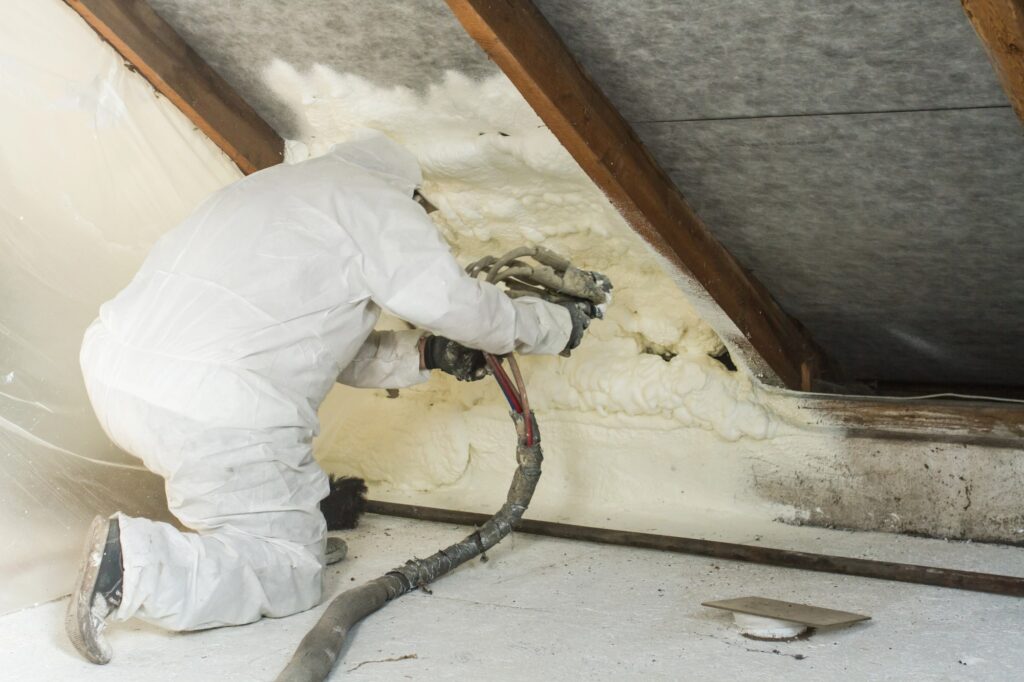 man in full PPE applying spray foam insulation to attic