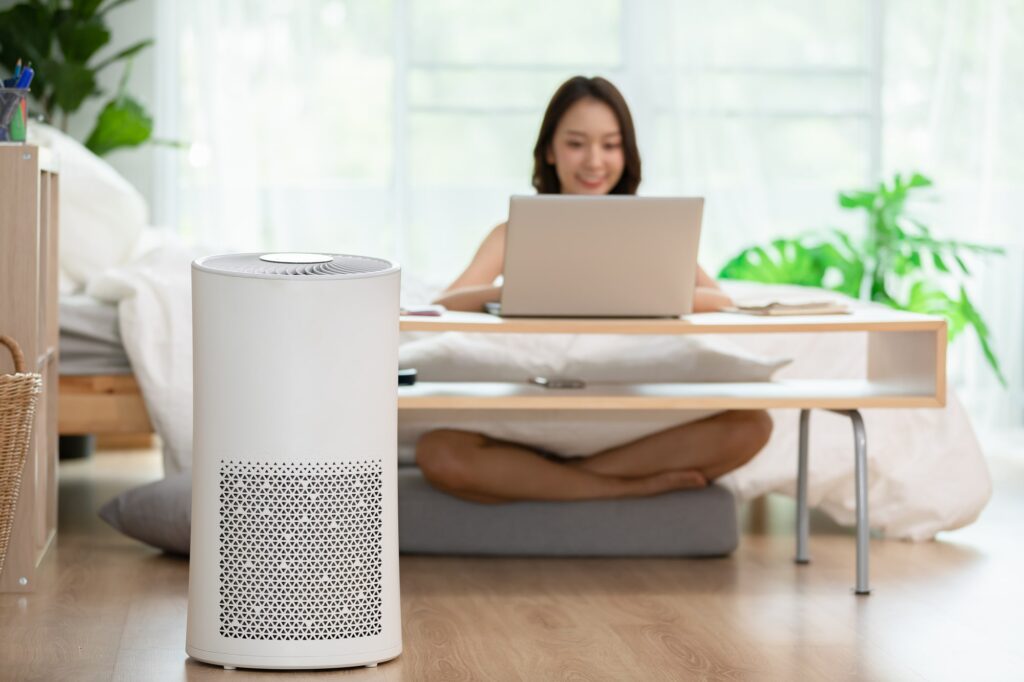 Air purifier in front of a happy female working in front of her laptop on her bed