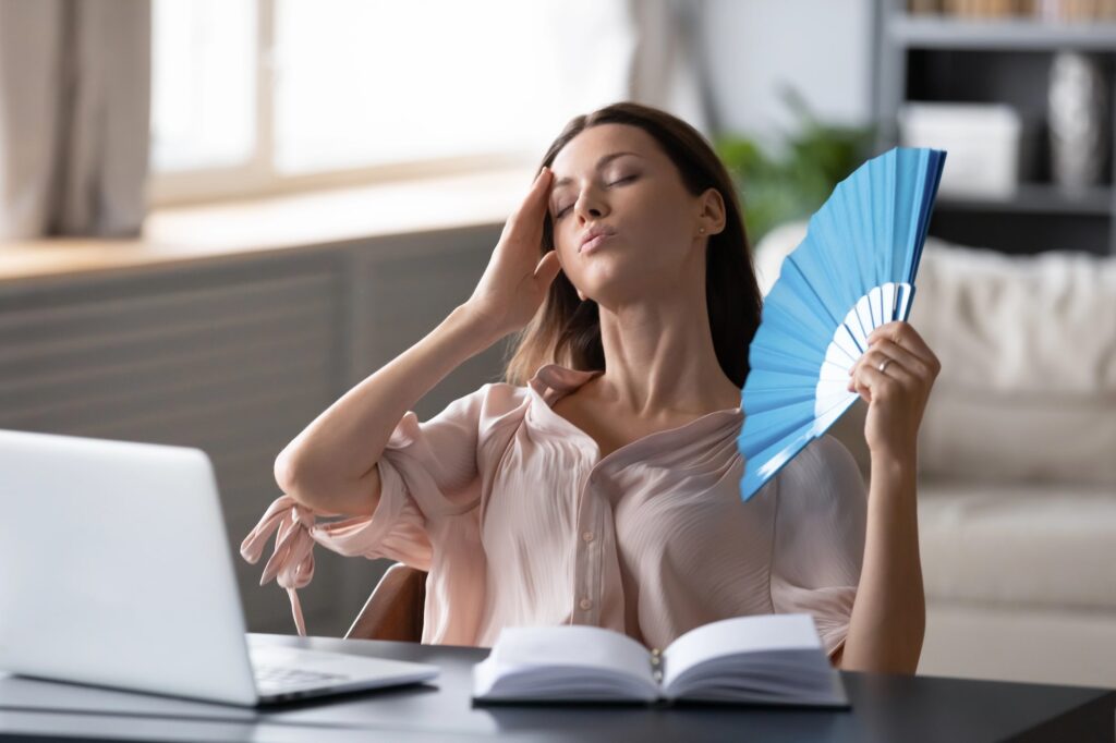 woman fanning herself because of the ac blowing hot air